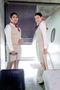 Two beautiful Asian female air hostesses walking with luggage with aircraft as background, flight attendant boarding a plane, Royalty Free Stock Photo