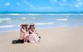Two beautiful Asian women with big hat enjoy spending time with friend on tropical sand beach blue sea together, sitting on  beach Royalty Free Stock Photo