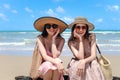 Two beautiful Asian women with big hat enjoy spending time with friend on tropical sand beach blue sea together, sitting on  beach Royalty Free Stock Photo