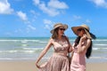 Two beautiful Asian women with big hat and sunglasses enjoy spending time with friend on tropical sand beach blue sea together, re Royalty Free Stock Photo