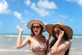 Two beautiful Asian women with big hat and sunglasses enjoy spending time with friend on tropical sand beach blue sea together, re Royalty Free Stock Photo