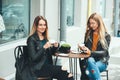 Two beautiful attractive stylish women are sitting outdoor in cafe drinking coffe and tea talking and enjoying great day.