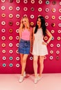 Two beautiful blonde and brunette girls closeup on the pink donut background