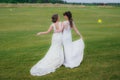 Two beautiful brides embracing on the green field