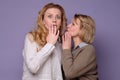 Two beautiful caucasian mature women telling secret on a colored background Royalty Free Stock Photo