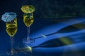 Two flute glasses with sparkling yellow liquid with colored paper umbrellas on top, cast reflections and shadows on a blue surface Royalty Free Stock Photo