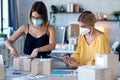 Two beautiful freelance business women seller wearing a hygienic facial mask while checking product order while packing and Royalty Free Stock Photo