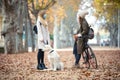 Two beautiful friends wearing surgical mask talking while walking with their dog and bike in the park in autumn. Social distance Royalty Free Stock Photo