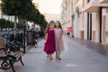 Two beautiful girlfriends with long flowing hair in beautiful dresses walking on a city street Royalty Free Stock Photo