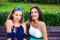 Two beautiful girlfriends are sitting on a bench in a summer park Royalty Free Stock Photo