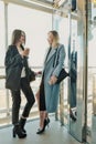 Two beautiful girls, a blonde and a brunette, are wearing a coat in a glass elevator with a window. Shopping center or Royalty Free Stock Photo