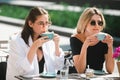 Two beautiful girls with cups coffee in summer cafe. Girl friends in cafe outdoor. Outdoors portrait of two young Royalty Free Stock Photo