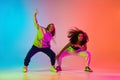 Two beautiful girls dancing hip-hop on colorful gradient background in neon lights Royalty Free Stock Photo