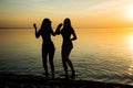 Two beautiful girls are dancing holding hands on the beach at sunset background, silhouettes Royalty Free Stock Photo