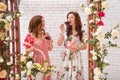 Two beautiful girls dressed in summer dresses near flower arch are drinking red wine. Royalty Free Stock Photo