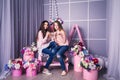 Two beautiful girls in jeans and pink sweaters are holding beads in studio with decor of flowers in baskets. Royalty Free Stock Photo