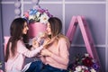 Two beautiful girls in jeans and pink sweaters are holding beads in studio with decor of flowers in baskets. Royalty Free Stock Photo