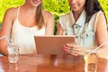 Two beautiful girls looking at tablet pc computer in cafe outside Royalty Free Stock Photo