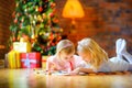 Two beautiful girls are lying on the floor near the Christmas tree and diligently writing a letter Royalty Free Stock Photo