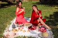 Two beautiful girls in red evening dresses  had a picnic in the park to celebrate the anniversary. Royalty Free Stock Photo