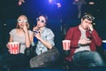 Two beautiful girls are sitting together. Blonde girl is eating popcorn while her friend is drinking coke. Guy is Royalty Free Stock Photo