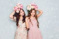 Two beautiful girls stand in a studio, play silly and have circlets of flowers on their heads. They wear light silk