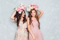 Two beautiful girls stand in a studio, play silly and have circlets of flowers on their heads. They wear light silk
