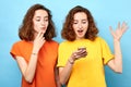 Two beautiful girls twins smiling, looking at smart phone over blue background. Royalty Free Stock Photo