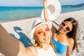 Two beautiful girls with white hats taking a self-portrait enjoying summer vacation on tropical beach resort. POV of young blonde Royalty Free Stock Photo