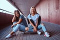 Two beautiful happy hipster girls sitting on skateboard at a sidewalk under bridge. Royalty Free Stock Photo