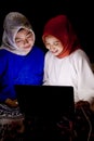 Two beautiful hijab ladies learning together by reading a book and browsing on a laptop.. Royalty Free Stock Photo