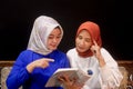 Two beautiful hijab ladies learning together by reading a book and browsing on a laptop.. Royalty Free Stock Photo