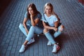 Two beautiful hipster girls sitting on a skateboard at a sidewalk under bridge. Royalty Free Stock Photo