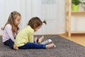 Two beautiful little sisters sit at a table and play on a tablet Royalty Free Stock Photo