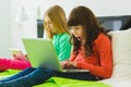 Two beautiful little sisters sitting on bed and play with a Tablet or laptop Royalty Free Stock Photo