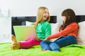 Two beautiful little sisters sitting on bed and play with a Tablet or laptop Royalty Free Stock Photo