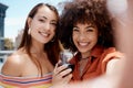 Two beautiful mix race women smiling taking a selfie while enjoying a glass of red wine while outdoors at a party Royalty Free Stock Photo