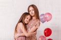 Two beautiful school-age girls in dress in a white room cuddle