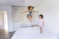 Two beautiful sister kids playing and jumping on bed at home. Fun indoors. Family love and lifestyle