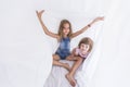 Two beautiful sister kids playing under white sheets on bed. Fun indoors. Family love and lifestyle