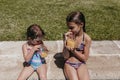 Two beautiful sister kids at the pool drinking healthy orange juice and having fun outdoors. Summertime and lifestyle concept