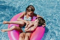 Two beautiful sisters floating on pink donuts in a pool. Playing tickles and smiling. Fun and summer lifestyle Royalty Free Stock Photo