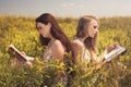 Two beautiful smiling girls reading book against yellow flowers