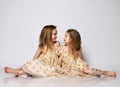 Two beautiful smiling kids girls sisters in same summer dresses with stars sitting on floor looking at each other Royalty Free Stock Photo