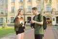 Two beautiful students guy and girl talking on background of university building, holding books, exercise books and laptop. A Royalty Free Stock Photo