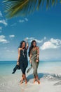 Two beautiful twin sisters in elegant dresses having fun on tropical beach Royalty Free Stock Photo