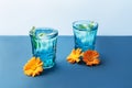 Two beautiful vintage blue glasses with cold drink and ice cubes, with fresh green mint leaves decorated with marigold