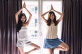 Two beautiful waked up roommate girls stretch body by yoga exercise near window during sunrise in early morning