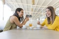 Two beautiful women having breakfast in a restaurant. They are laughing and searching information on mobile phone. Indoors Royalty Free Stock Photo