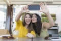 Two beautiful women having breakfast in a restaurant and taking a selfie with mobile phone. They are laughing. Indoors lifestyle Royalty Free Stock Photo